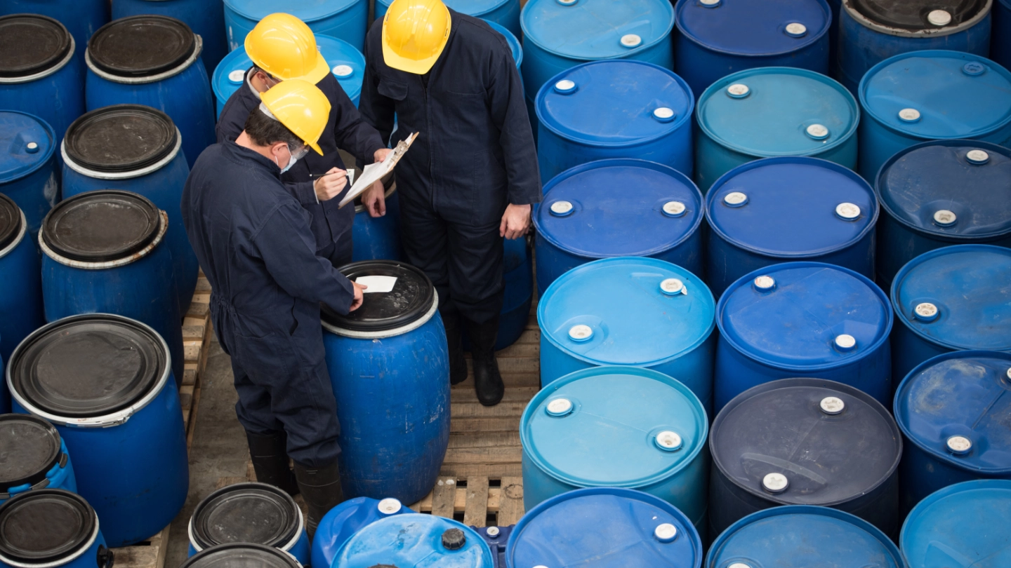 Three men inspecting chemical drums Three men inspecting chemical drums